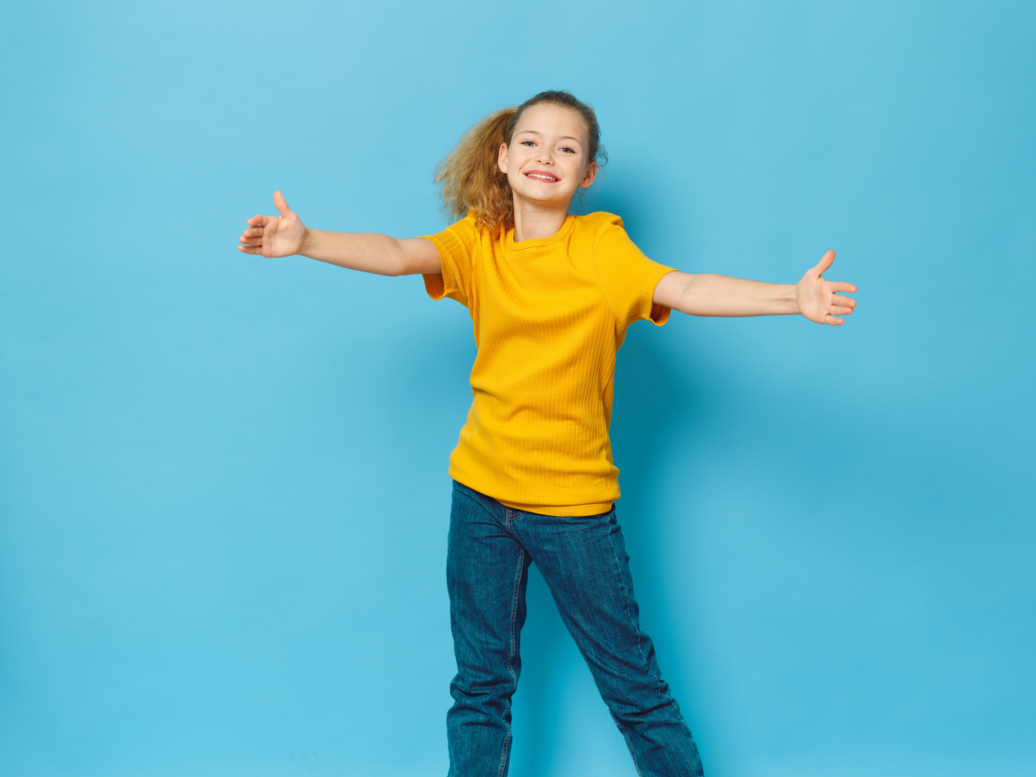 Girl in Yellow Shirt with Open Arms on Blue Background